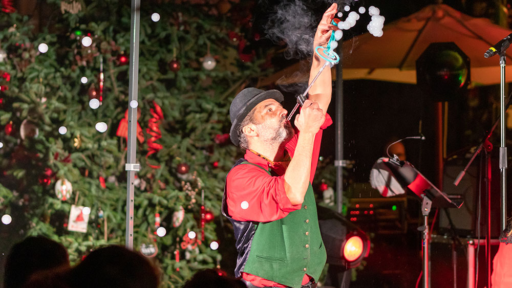 Ένας άνδρας με χριστουγεννιάτικη ενδυμασία χρησιμοποιεί μια συσκευή για να φυσήξει φούσκες στον αέρα