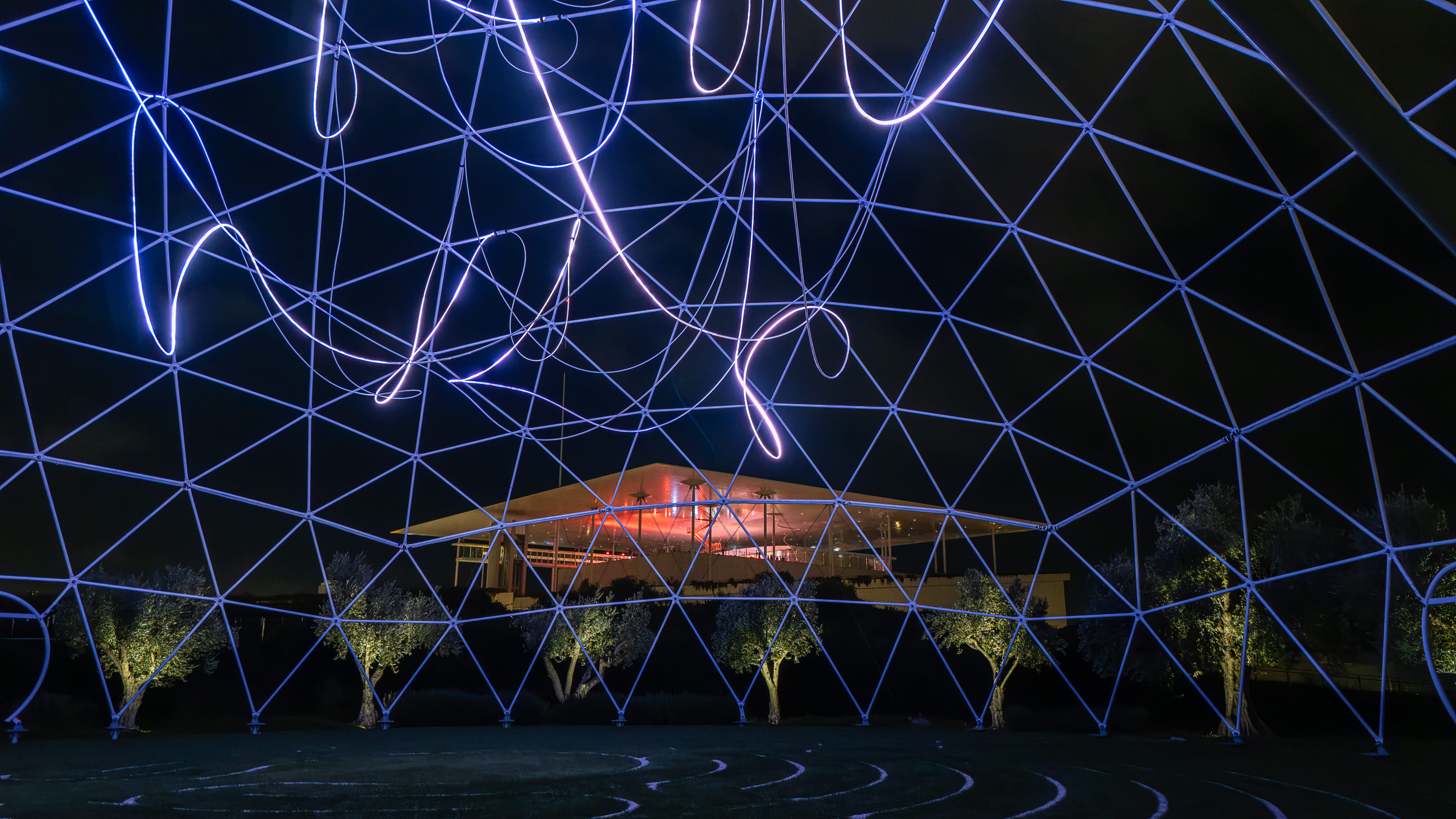 Ο Θόλος την νύχτα με μια μεγάλη φωτιστική εγκατάσταση να κρέμεται από την οροφή του, με το ΚΠΙΣΝ να φαίνεται στο βάθος.