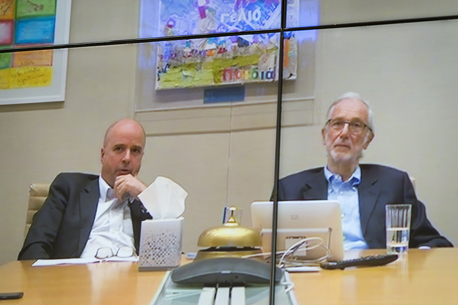 Κοντινή φωτογραφία από μια διαδικτυακή σύνδεση η οποία δείχνει τον Αντρέα Δρακόπουλο, Πρόεδρο του Ιδρύματος Σταύρος Νιάρχος να κάθεται δίπλα με έναν άλλον άντρα σε λενα τραπέζι συνεδριάσεων 