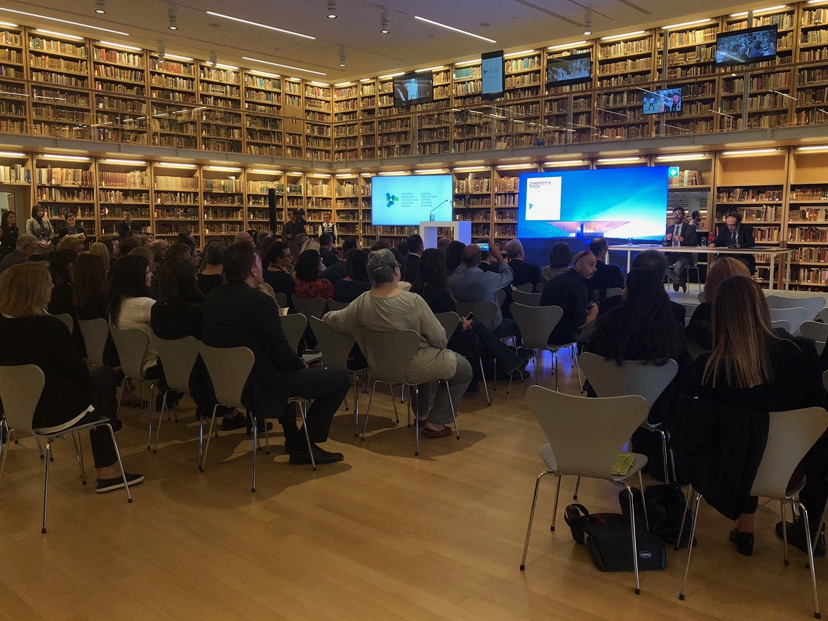 Κόσμος κάθεται σε καρέκλες και περιμένει να αρχίσει η ομιλία