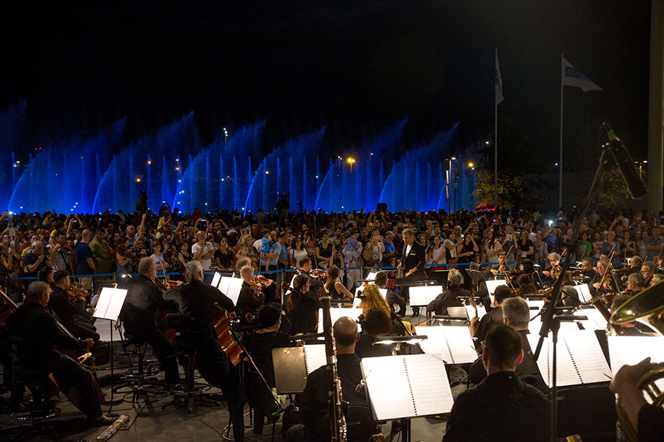 Μια ορχήστρα παίζει σε εξωτερικό χώρο και πλήθος ανθρώπων έχουν μαζευτεί για να τους ακούσουν