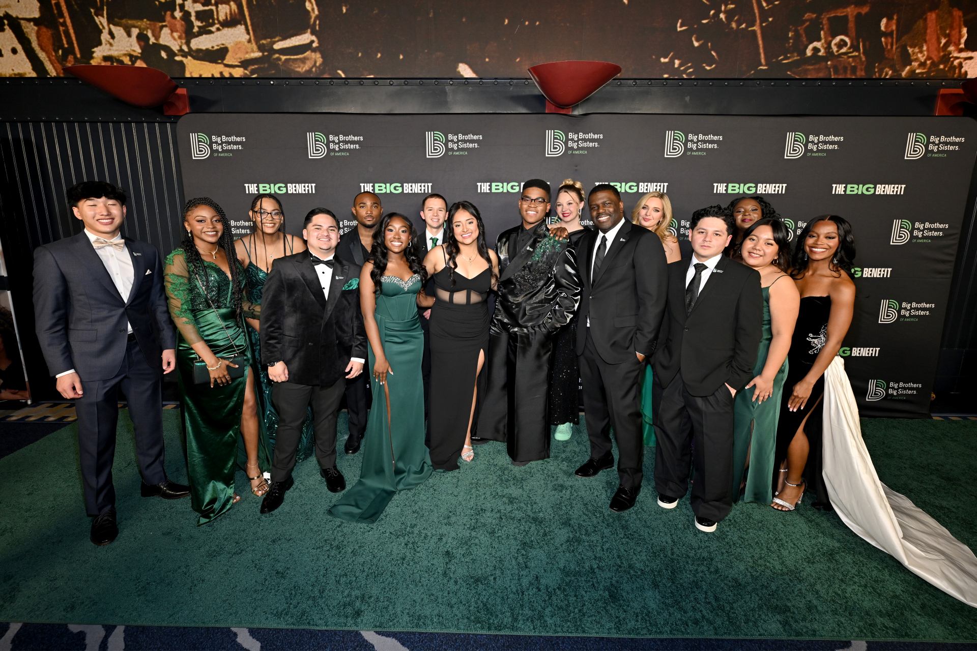 Μια ομάδα νέων ανθρώπων  στέκεται πάνω σε ένα πράσινο χαλί και ποζάρει χαμογελαστά για μια φωτογραφία. 