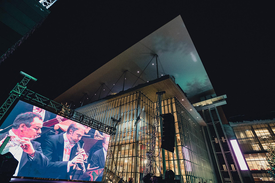 Η πλευρά του Κέντρου Πολιτισμού Ίδρυμα Σταύρος Νιάρχος με μια μεγάλη οθόνη που δείχνει δύο μουσικούς να παίζουν τα όργανά τους