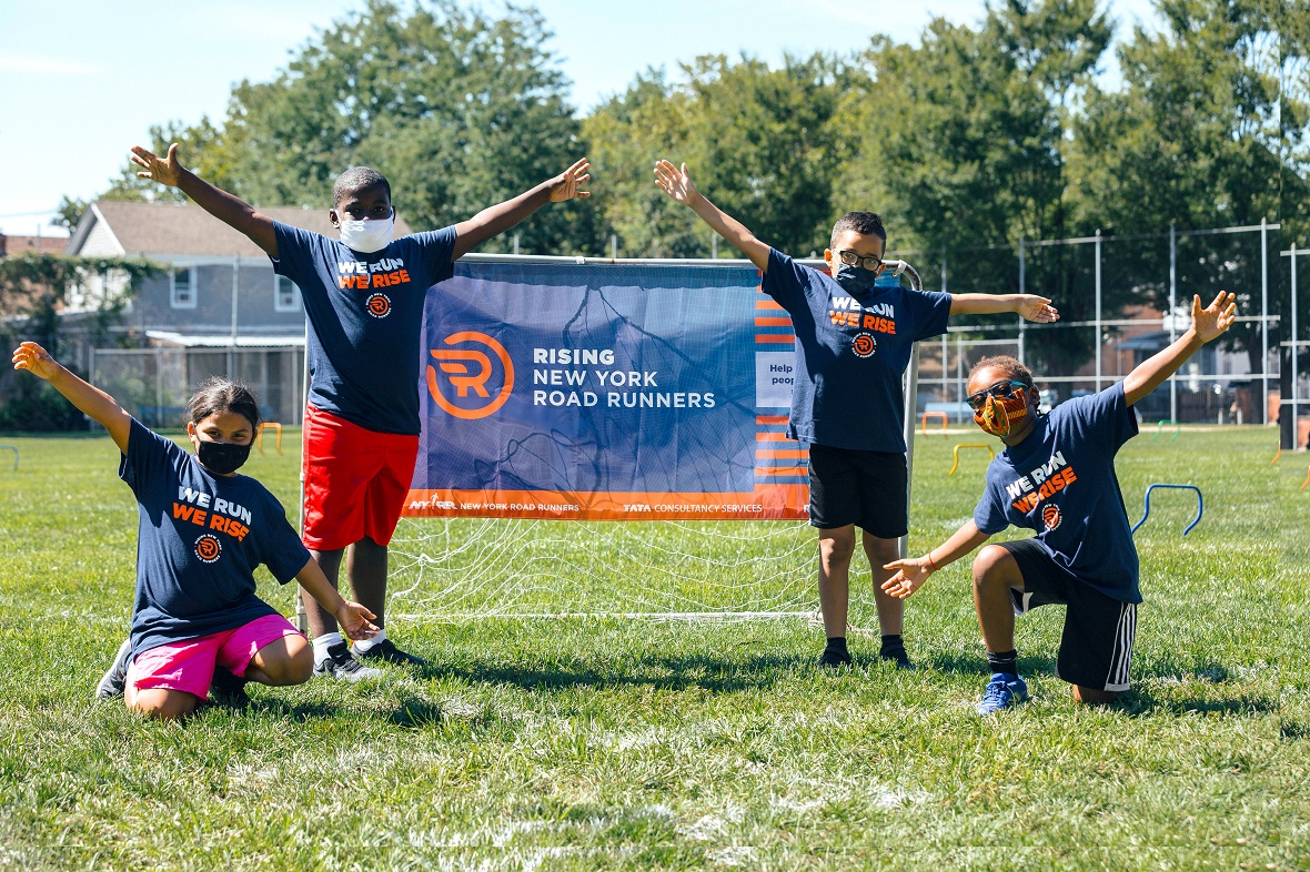 Μια ομάδα τεσσάρων ατόμων σε ένα γήπεδο ποδοσφαίρου ποζάρουν σηκώνοντας τα χέρια ψηλά δίπλα σε ένα τέρμα που γράφει 