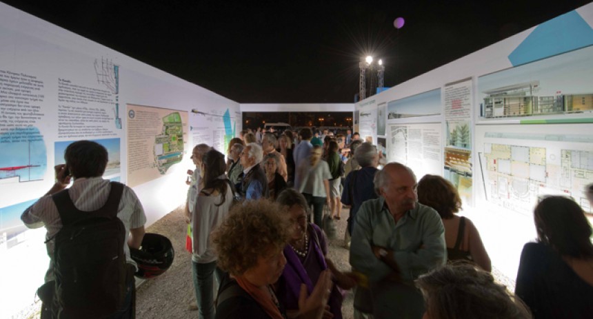 Κόσμος περπατάει σε έναν διάδρομο και κοιτάει τα σχέδια και τα υπομνήματα που υπάρχουν στους τοίχους