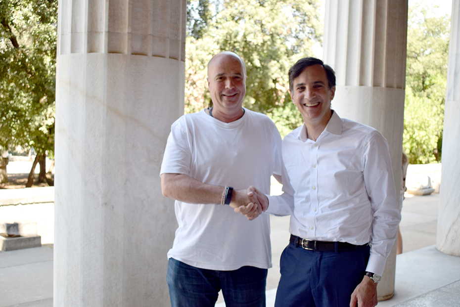 Ο Ανδρέας Δρακόπουλος και ένας άλλος άνδρας χαμογελούν και σφίγγουν τα χέρια σε ένα αρχαιολογικό μουσείο