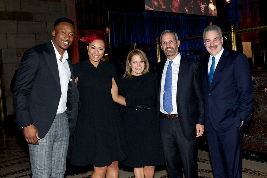 Τρεις άντρες και δύο γυναίκες στέκονται αγκαλισμένοι για μια αναμνηστική φωτογραφία 