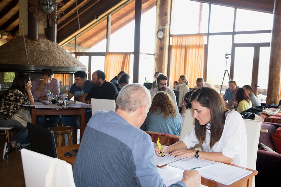 Φωτογραφία που δείχνει πολλές ομάδες να κάθονται σε ξεχωριστά τραπέζια και να σχειάζουν σε χαρτιά