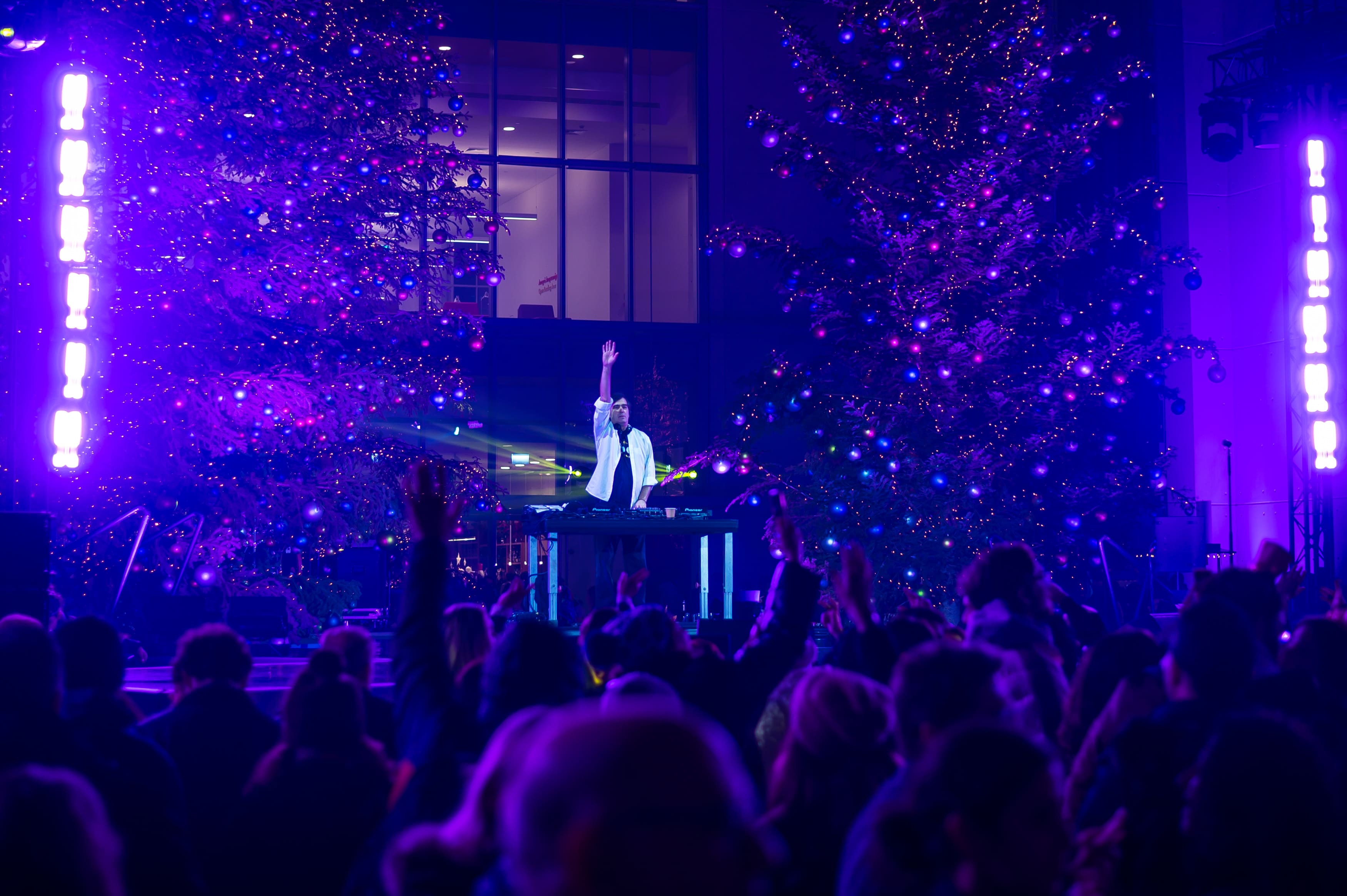 Ένας DJ που σηκώνει το χέρι του στη σκηνή του ΚΠΙΣΝ, μπροστά στο κοινό και σε δυνατά φώτα.