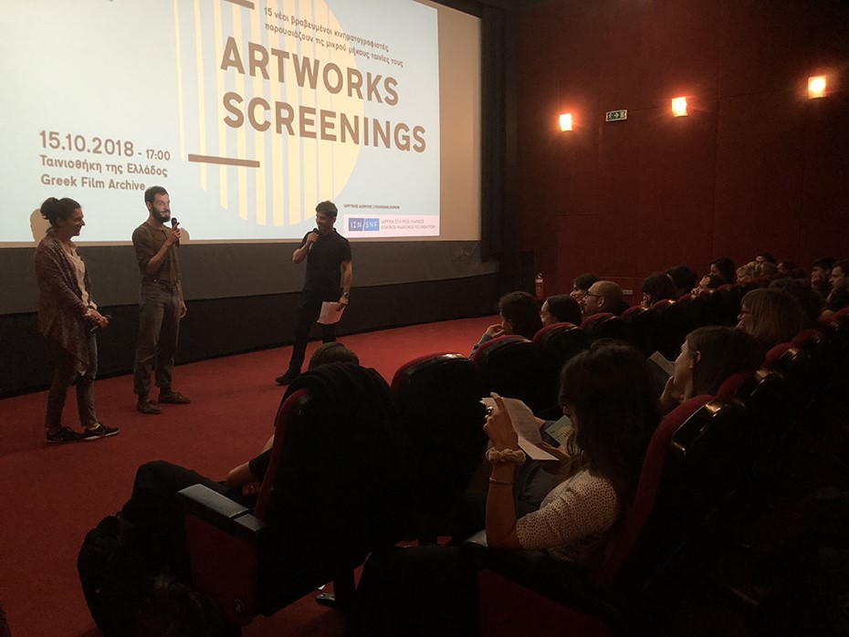 Δύο άντρες και μια γυναίκα είναι στη σκηνή κρατώντας ένα μικρόφωνο στο χέρι και ο κόσμος κάθεται σε καρέκλες και τους παρακολουθεί 