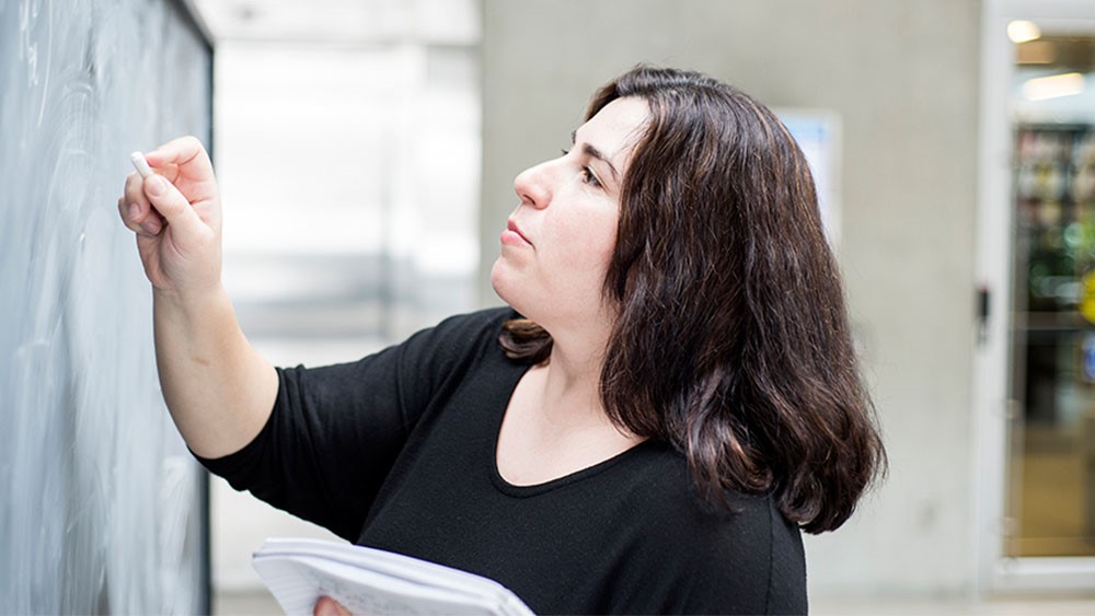 Μια γυναίκα γράφει σε έναν πίνακα με κιμωλία.