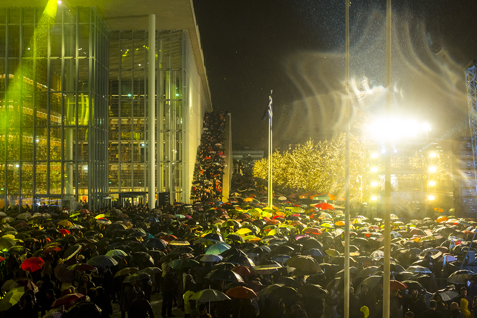 Πλήθος κόσμου συγκεντρώνεται με ομπρέλες έξω από το Κέντρο Πολιτισμού Ίδρυμα Σταύρος Νιάρχος
