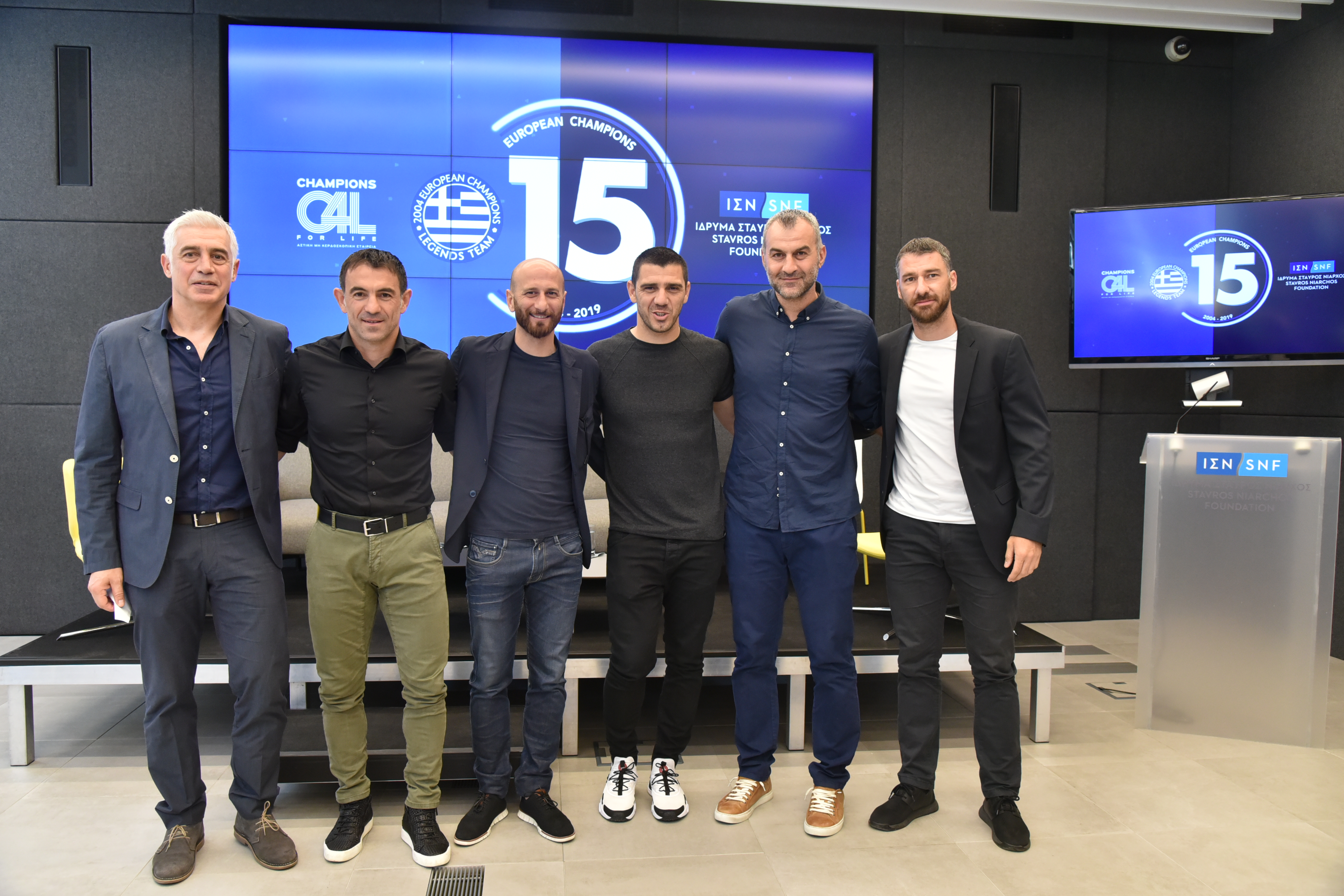 Έξι άντρες στέκονται όρθιοι και αγκαλιάζονται για μια αναμνηστική φωτογραφία