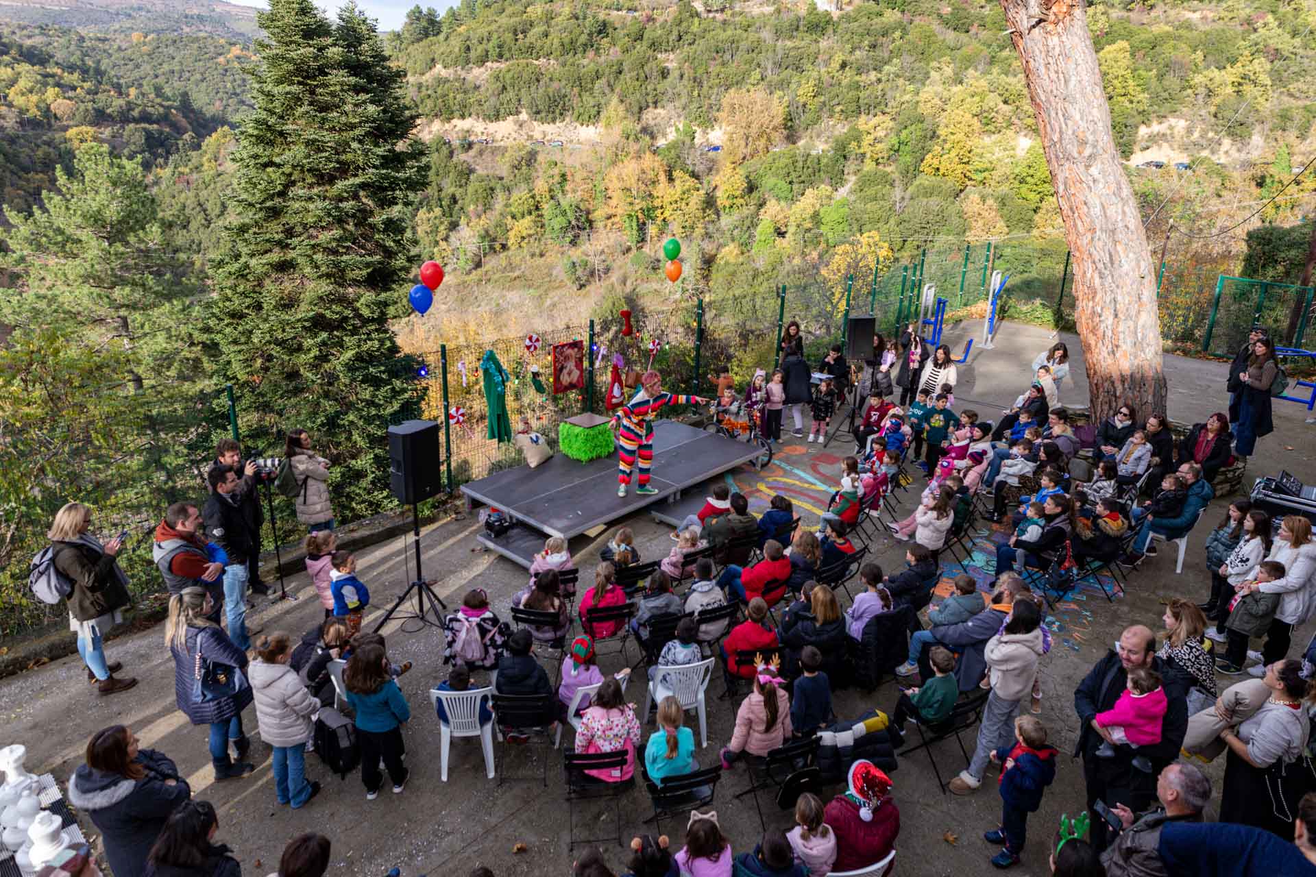 Γυναίκα ντυμένη με πολύχρωμα ρούχα πάνω στη σκηνή απευθύνεται στα παιδιά και τους γονείς που κάθονται και την παρακολουθούν με φόντο το βουνό του Πάρνωνα.