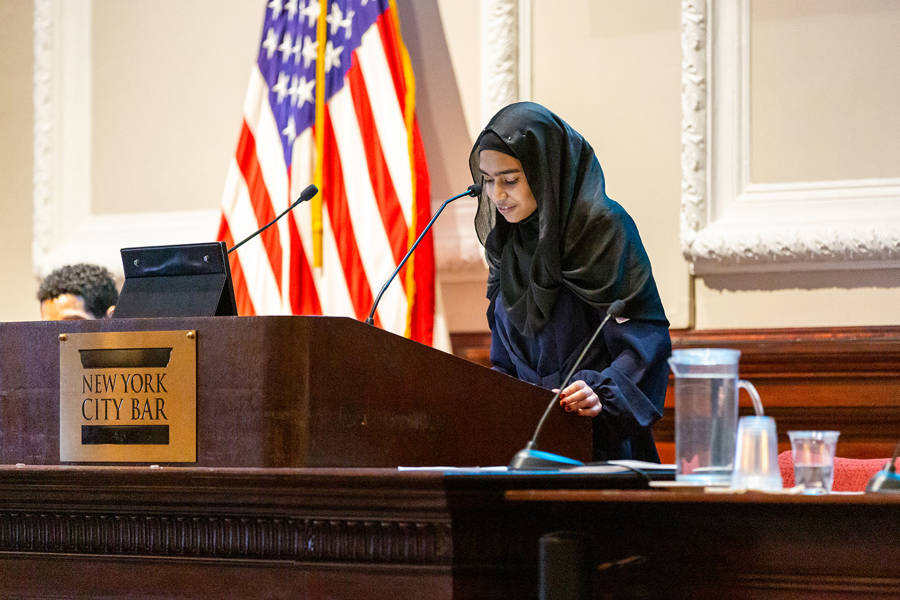 A high school student speaks from a podium that reads “New York City Bar.”