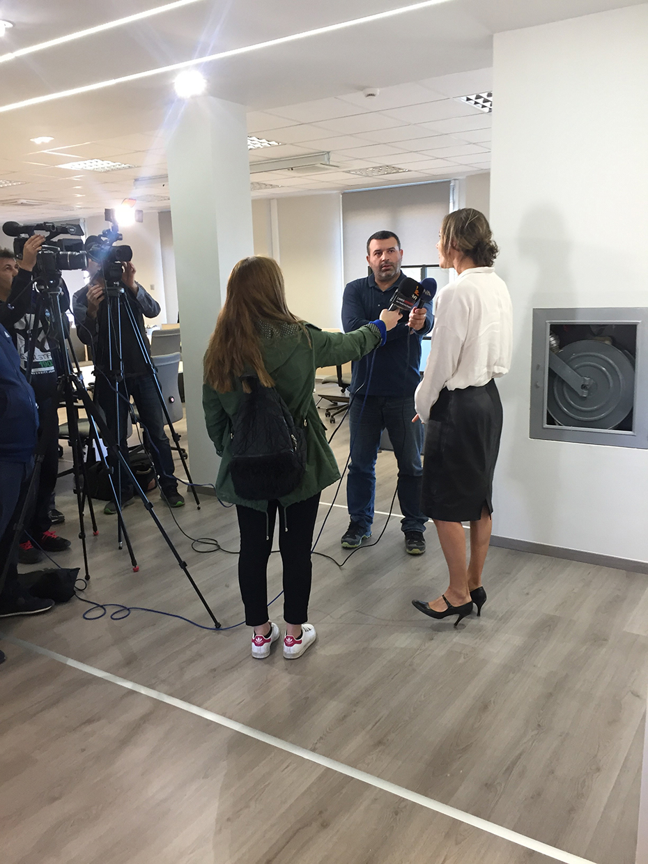 Μια γυναίκα μιλάει σε μικρόφωνα που κρατούν δύο άτομα και βιντεοσκοπείται από πολλές κάμερες