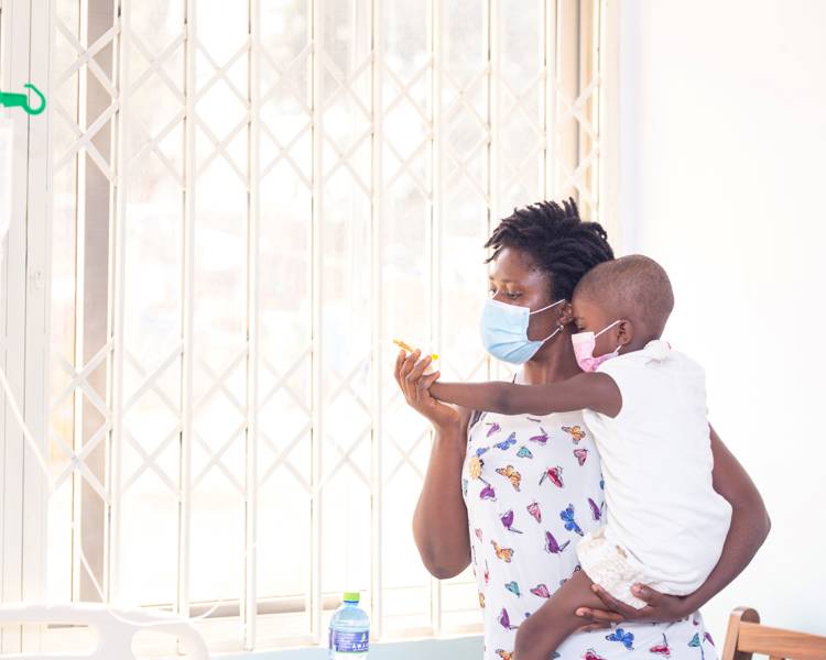 Μία γυναίκα που κρατάει ένα παιδί. Και οι δύο φορούν προστατευτικές μάσκες προσώπου.