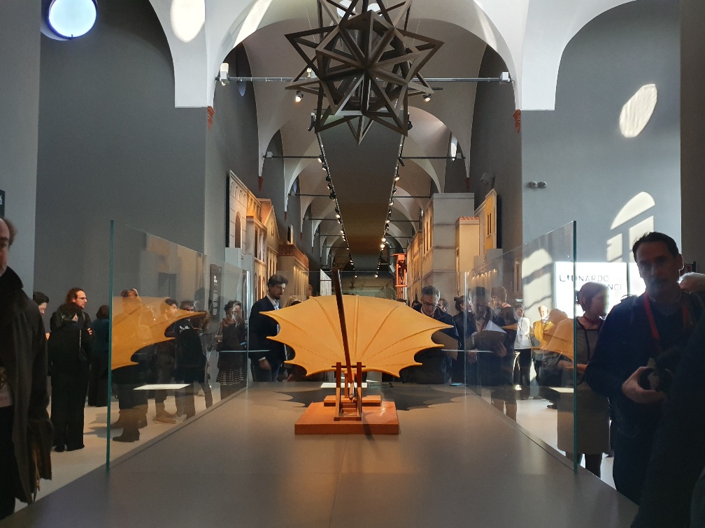 Φωτογραφία που δείχνει ένα έργο τέχνης το οποίο μοιάζει σαν ένα μηχάνημα να προσπαθεί να σηκώσει ένα μεγάλο πλατανόφυλλο και γύρω ο κόσμος το κοιτάζει 