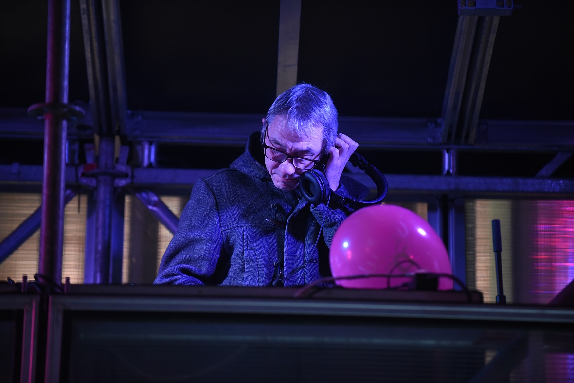 Ένας DJ κρατάει με το ένα χέρι τα ακουστικά του στο αυτί του και με το άλλο χέρι ελέγχει την κοσνόλα 