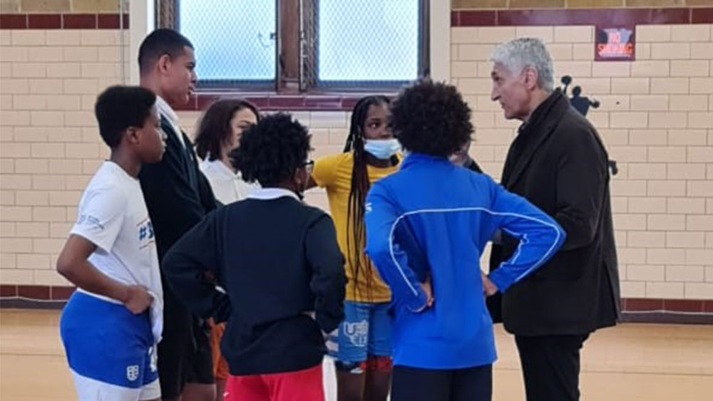 Πέντε παιδιά στέκονται σε κύκλο γύρω από έναν προπονητή σε ένα γήπεδο μπάσκετ