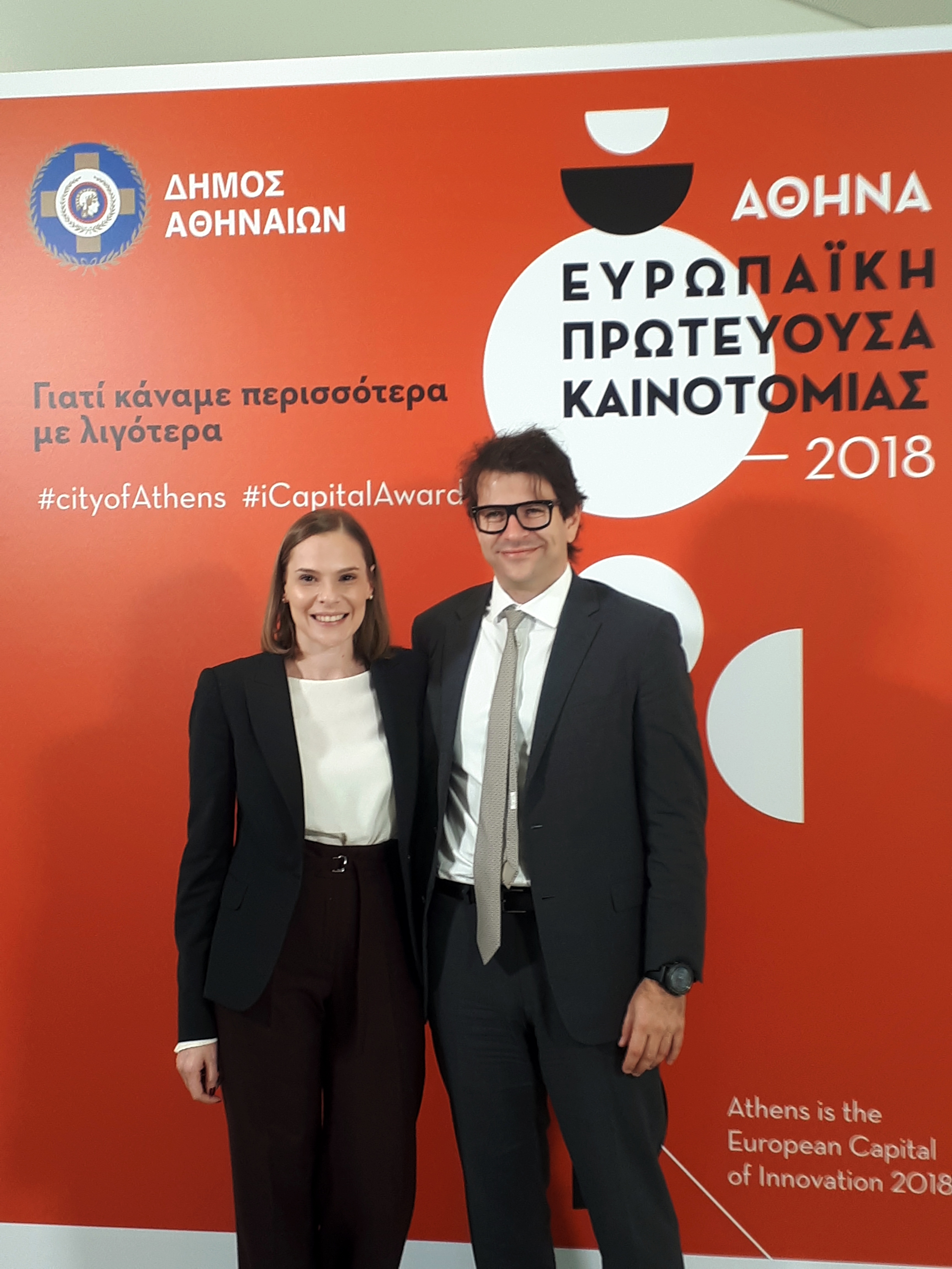 Ένας άντρας και μια γυναίκα φωτογραφίζονται μπροστά από το baner που γράφει ΑΘΗΝΑ ΕΥΡΩΠΑΙΚΗ ΠΡΩΤΕΥΟΥΣΑ ΚΑΙΝΟΤΟΜΙΑΣ 2018