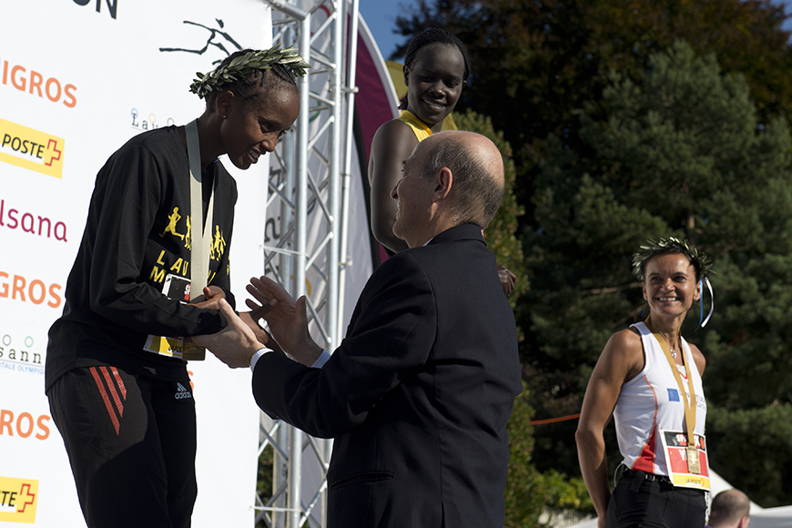 Μια αθλήτρια που φοράει ένα στεφάνιο από φύλλα δάφνης και έχει κερδίσει ένα μετάλιο κάνει χειραψία με έναν άντρα την ώρα που είναι στο βάθρο 