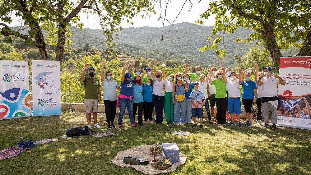 Οι αθλητές των Special Olympics Hellas και οι γονείς τους χαιρετούν την κάμερα μπροστά σε μια γραφική θέα του βουνού