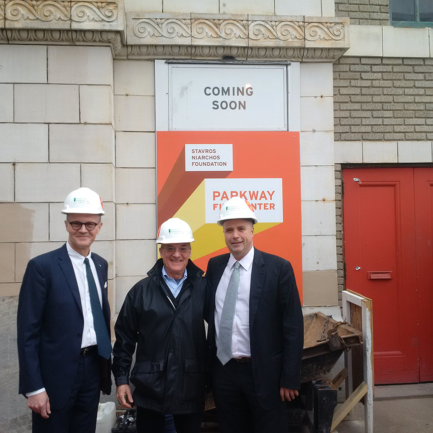 Ο Ανδρέας Δρακόπουλος, πρόεδρος του Ιδρύματος Σταύρος Νιάρχος, και δύο άλλοι άνδρες στέκονται με κατασκευαστικά καπέλα στο θέατρο Parkway