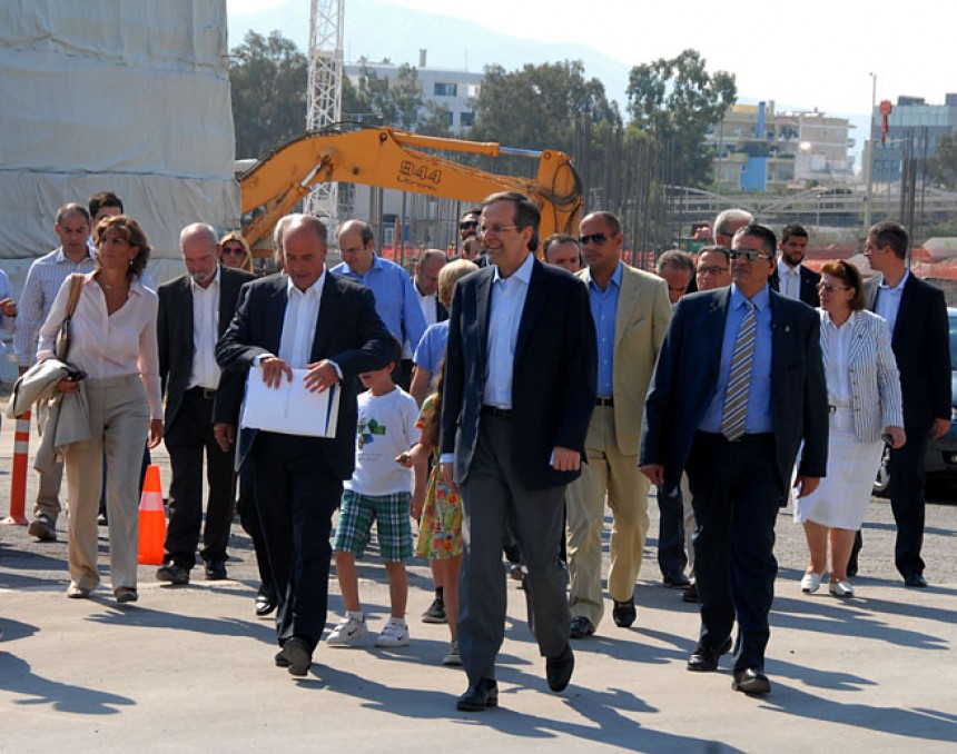 Ο Αντώνης Σαμαράς, πρωθυπουργός της Ελληνικής Δημοκρατίας, περπατά δίπλα στον Ανδρέα Δρακόπουλο, πρόεδρο του Ιδρύματος Σταύρος Νιάρχος, μπροστά σε άλλους ανθρώπους και δύο παιδιά, στο εργοτάξιο του Κέντρου Πολιτισμού του Ιδρύματος Σταύρος Νιάρχος