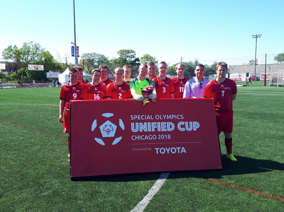 Μια ομάδα αντρών ντυμένων με την ίδια ποδοσφαιρική στολή κρατούν ένα πανό που γράφει Special Olympics unified cup Chicago 2018 και φωτογραφίζονται στο γήπεδο