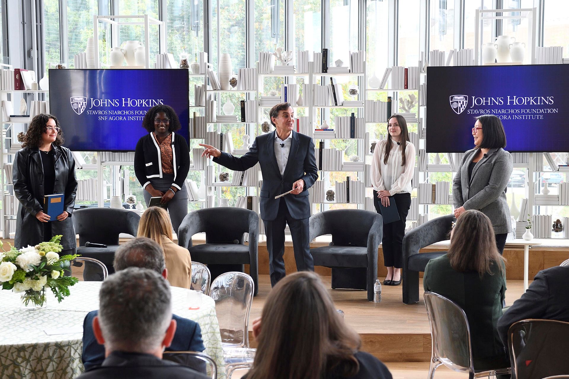One man speaks on stage with four participants during an SNF Agora Institute event