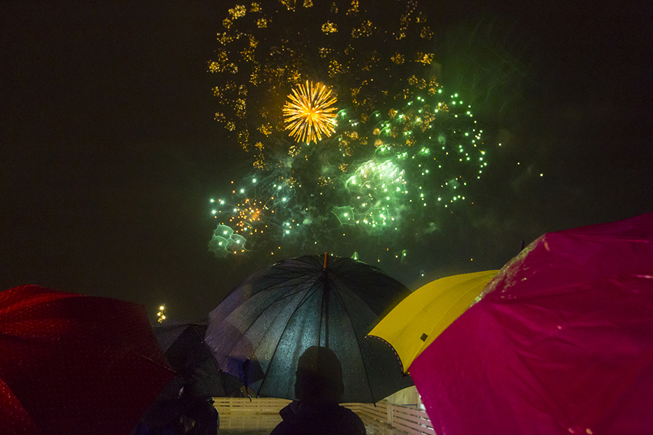 Άνθρωποι με ομπρέλες παρακολουθούν τα πυροτεχνήματα στο Κέντρο Πολιτισμού Ίδρυμα Σταύρος Νιάρχος