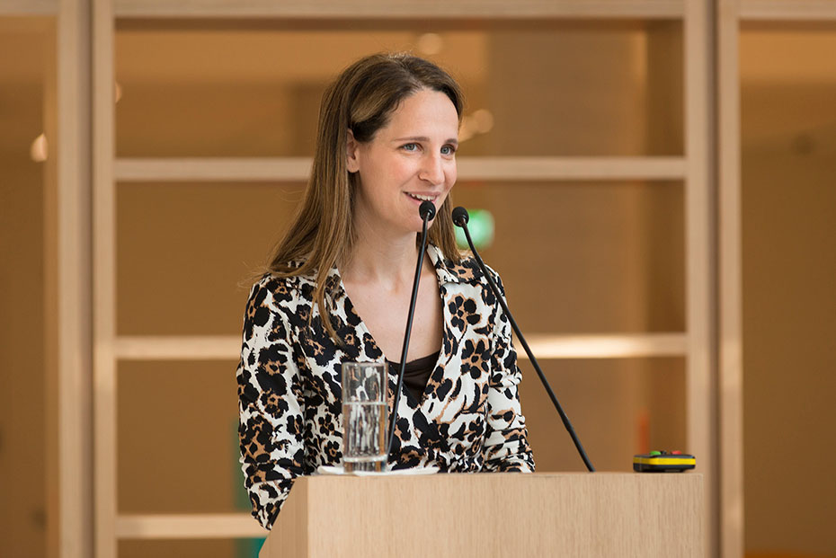 Μια γυναίκα χαμογελάει ενώ μιλάει σε ένα βήμα