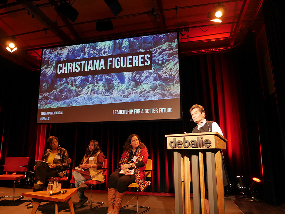 Τρεις γυναίκες κάθονται και μιλούν στη σκηνή, ενώ ο οικοδεσπότης της εκδήλωσης στέκεται πίσω από το βήμα και κοιτάζει το κοινό