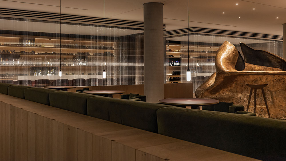 Ο εσωτερικός χώρος ενός εστιατορίου όπου φαίνονται χρυσά, ογκώδη έργα τέχνης, μια διαφανής κουρτίνα από κλωστές φωτός και στρογγυλά τραπέζια 