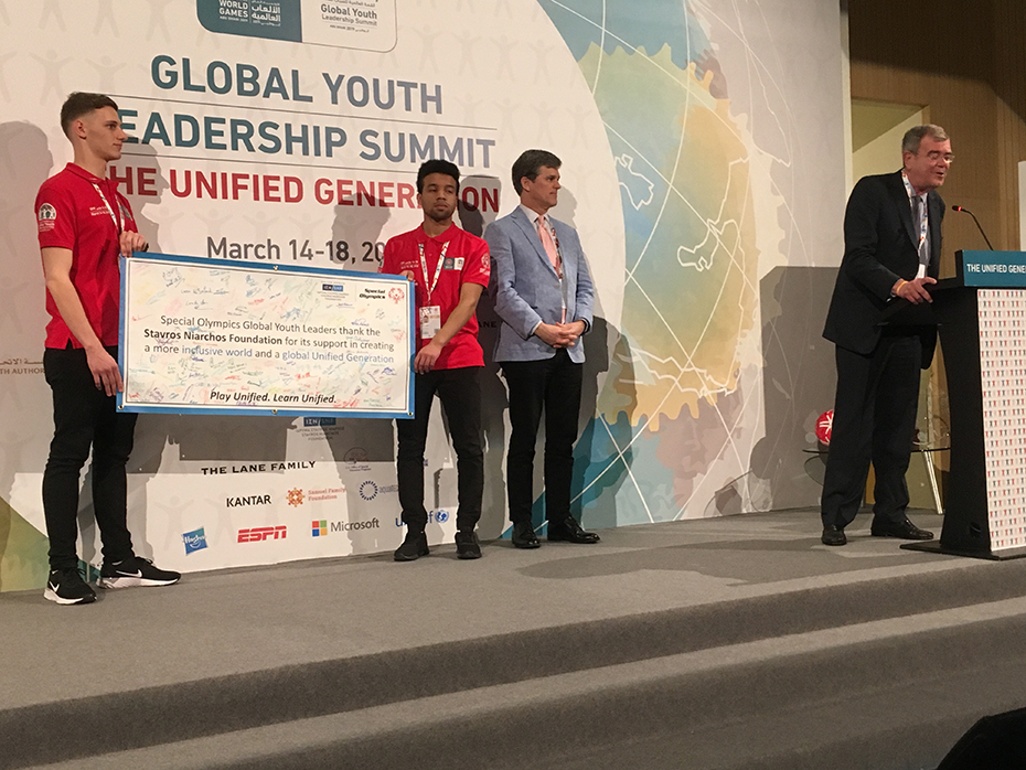 Two young men hold up a large check that writes 