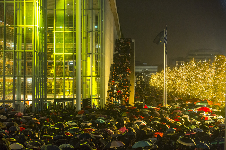Πλήθος κόσμου με ομπρέλες συγκεντρώνεται έξω από το Κέντρο Πολιτισμού Ίδρυμα Σταύρος Νιάρχος