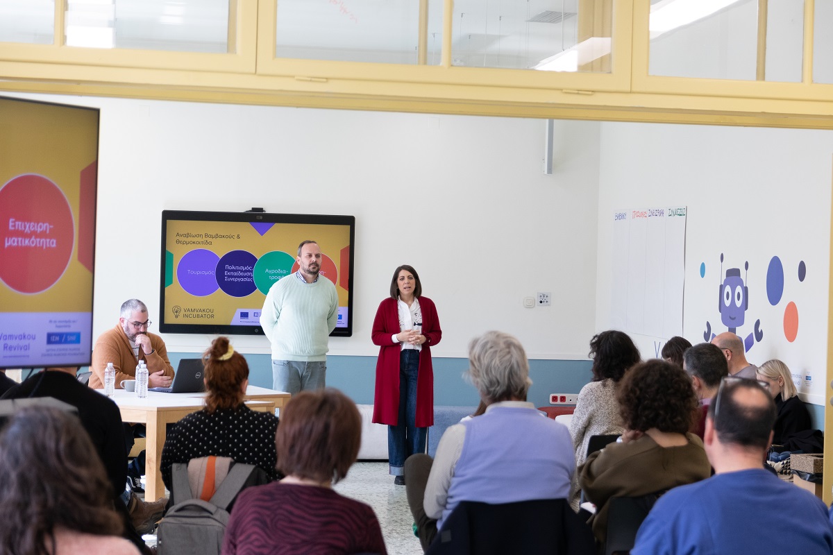 Δύο άνθρωποι κάνουν παρουσίαση μπροστά από το καθισμένο κοινό