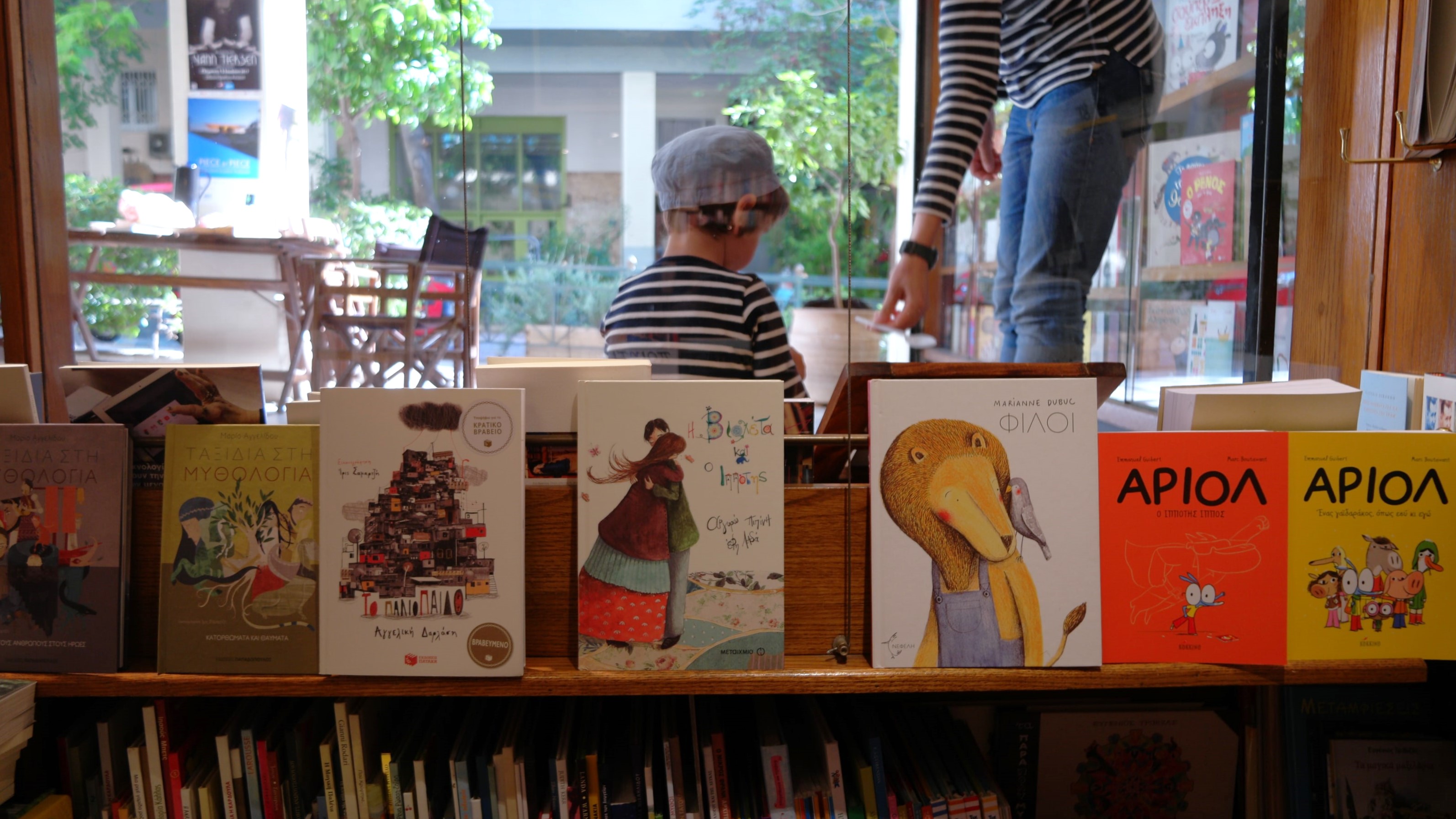Παιδικά βιβλία τοποθετιμένα πάνω σε ένα ράφι, ενώ στο παρασκήνιο ένα παιδί είναι μπροστά από το μαγαζί
