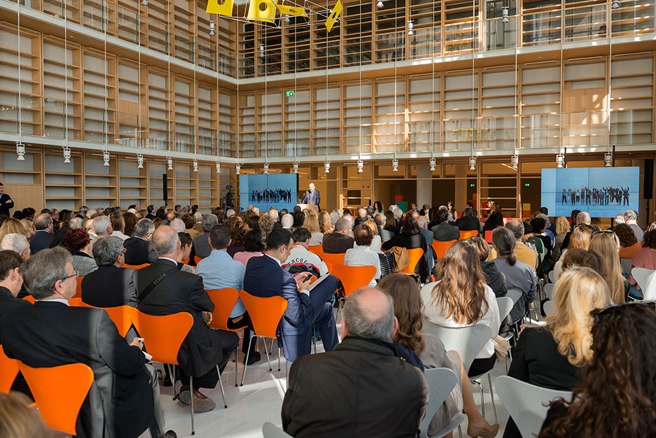 Το κοινό κάθεται σε καρέκλες στην Εθνική Βιβλιοθήκη και παρακολουθεί την παρουσίαση στο μπροστινό μέρος της αίθουσας