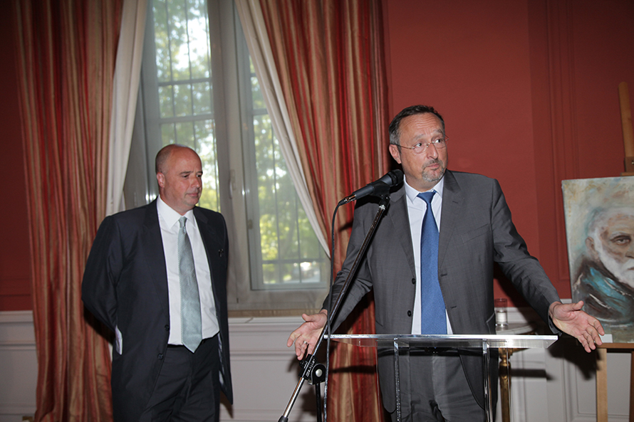 Ο Ανδρέας Δρακόπουλος, πρόεδρος του Ιδρύματος Σταύρος Νιάρχος, στέκεται δίπλα σε έναν άνδρα που δίνει ομιλία πίσω από ένα βήμα