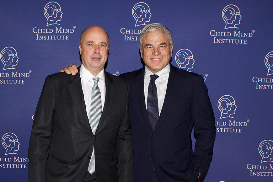 Ο Αντρέας Δρακόπουλος, Πρόεδρος του Ιδρύματος Σταύρος Νιάρχος, μαζί με έναν άλλον άντρα στέκονται αγκαλιασμένοικαι χαμογελούν μπροστά από ένα Banner που γράφει child mind institute για μια αναμνηστική φωτογραφία
