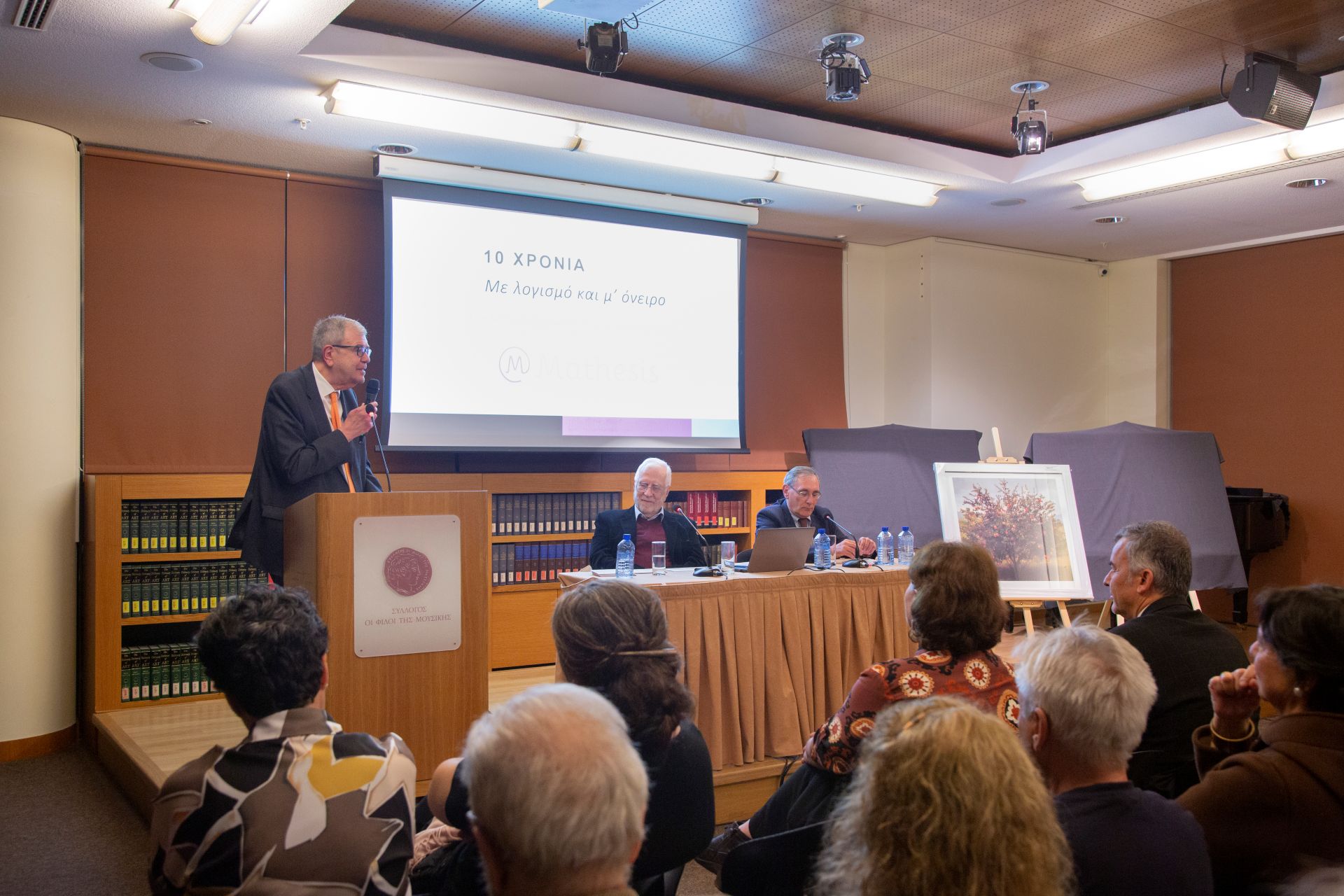 Event hall with audience listening to a speaker at a podium and panelists seated at a table with a screen above them reading 10 years