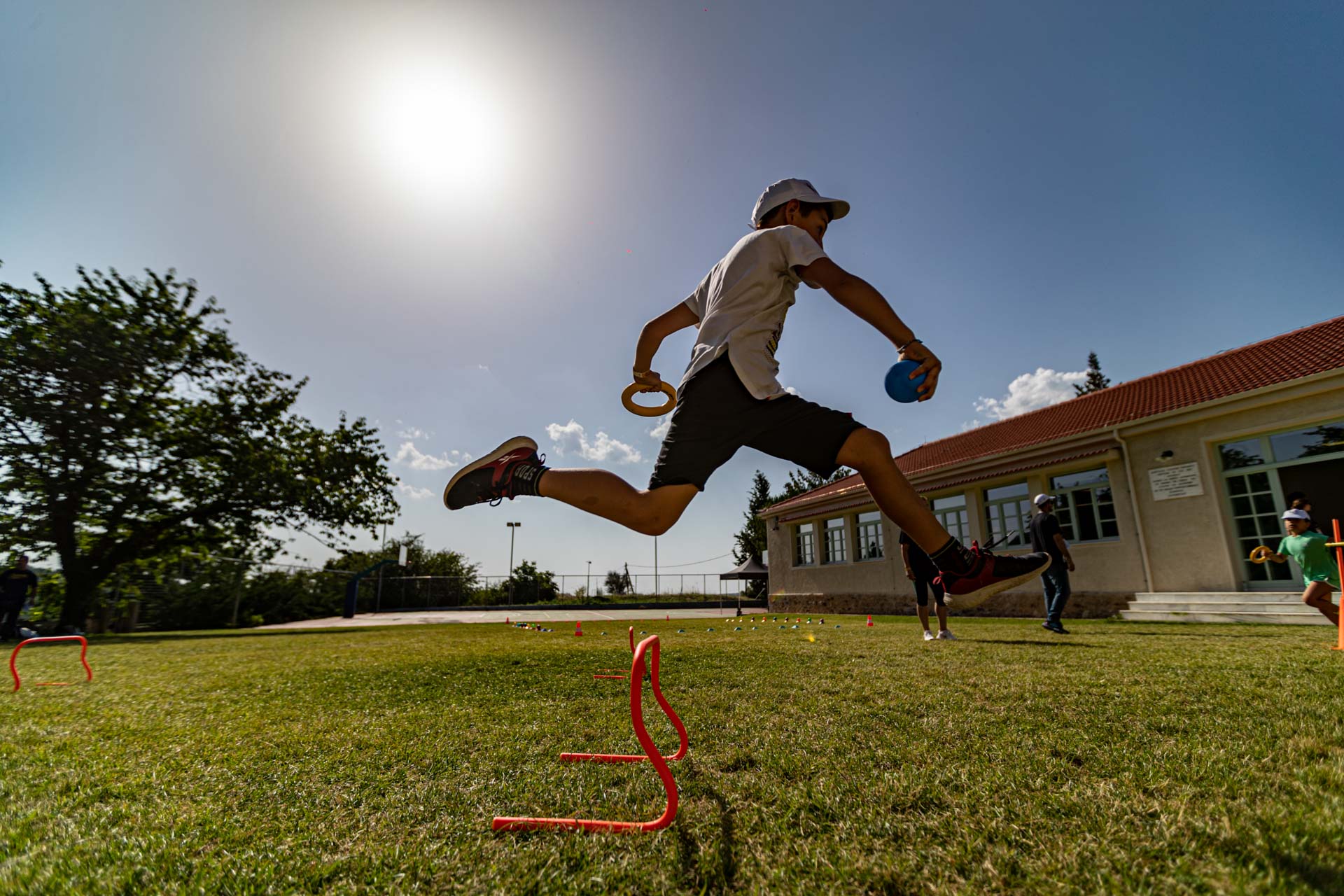 Ένα παιδί κρατώντας μια μπάλα και ένα δισκίο, πηδάει πάνω από ένα εμπόδιο γυμναστικής 