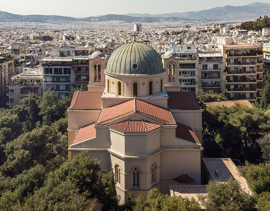 Μια εκκλησία ανάμεσα σε δέντρα μπροστά από μια μακρινή θέα της Αθήνας