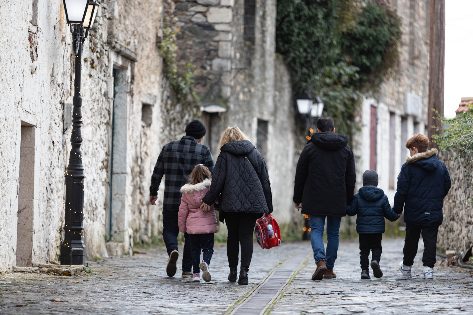 Τρεις γονείς με τα τρία παιδιά τους περπατούν σε ένα πέτρινο δρομάκι του χωριού. 