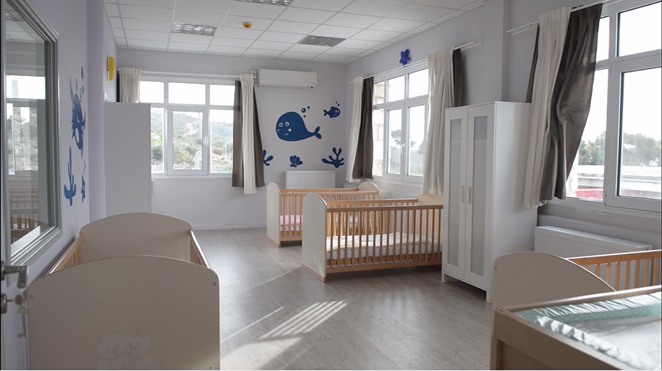 Ένα μωρουδιακό δωμάτιο στο οποίο υπάρχουν μωρουδιακές κούνιες , λευκές ντουλάπες και στους τοίχους υπάρχουν φάλαινες και ψαράκια