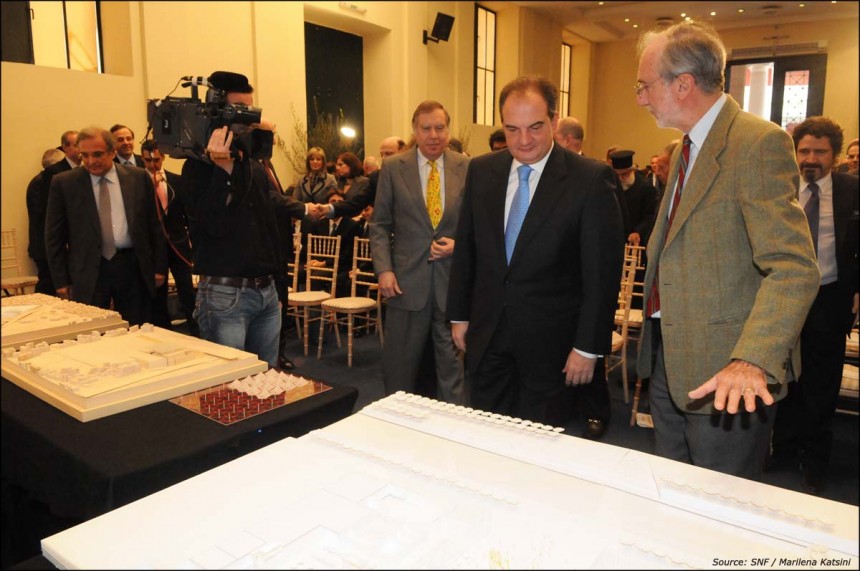 Δύο άντρες κοιτάζουν τα σχέδια σε κάποιες μακέτες και ο φωτογράφος τους βγάζει βίντεο και ο κόσμος τους κοιτά