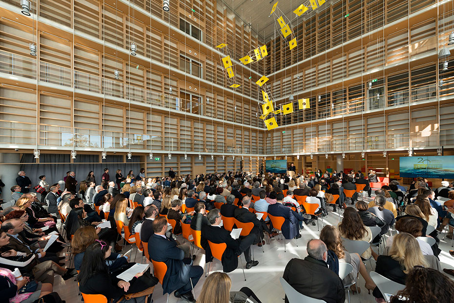 Ο κεντρικός χώρος της Εθνικής Βιβλιοθήκης είναι γεμάτος με ανθρώπους που κάθονται σε καρέκλες απέναντι από το βήμα