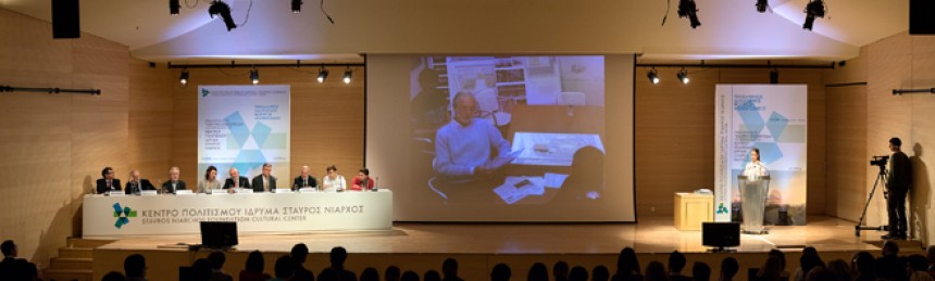 Εννέα άτομα κάθονται σε ένα τραπέζι συνεδριάσεων στη σκηνή του Κέντρου Πολιτισμού Ίδρυμα Σταύρος Νιάρχος